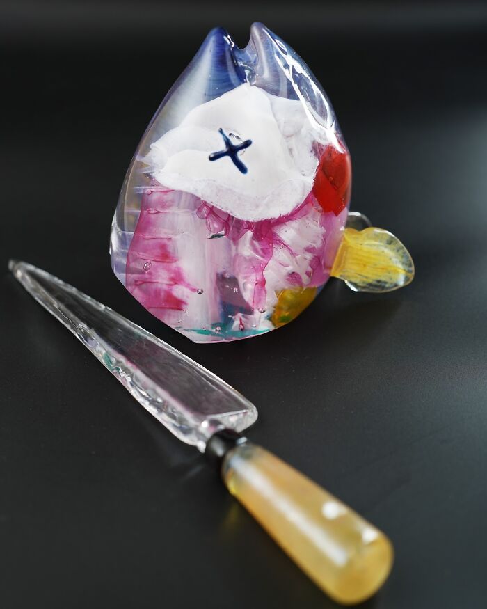 Hyper-realistic glass fish sculpture with an X mark and a glass knife, looking good enough to eat.