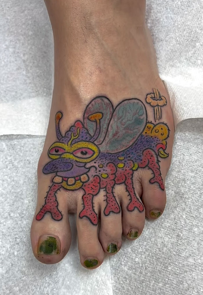 A tattoo artist's talent is displayed on a foot with a colorful cartoon bug tattoo, a questionable idea.