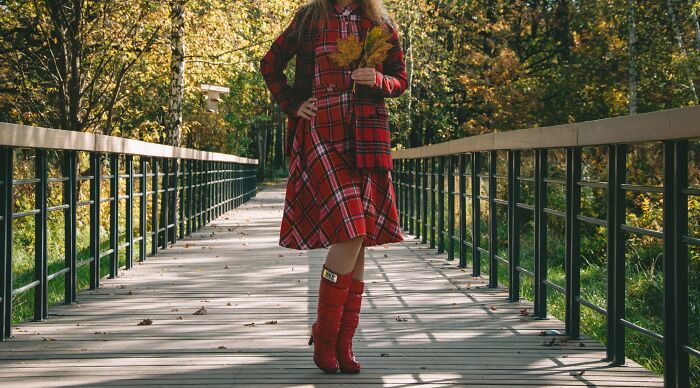 Woman wearing a red plaid dress and boots standing on a bridge in autumn Woman wearing a red plaid dress and boots standing on a bridge in autumn