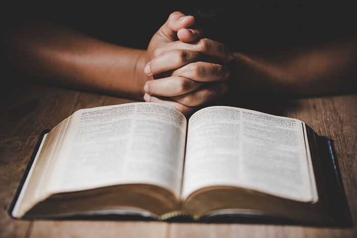 A person with clasped hands praying over an open Bible, illustrating disturbing things people learn about friends.