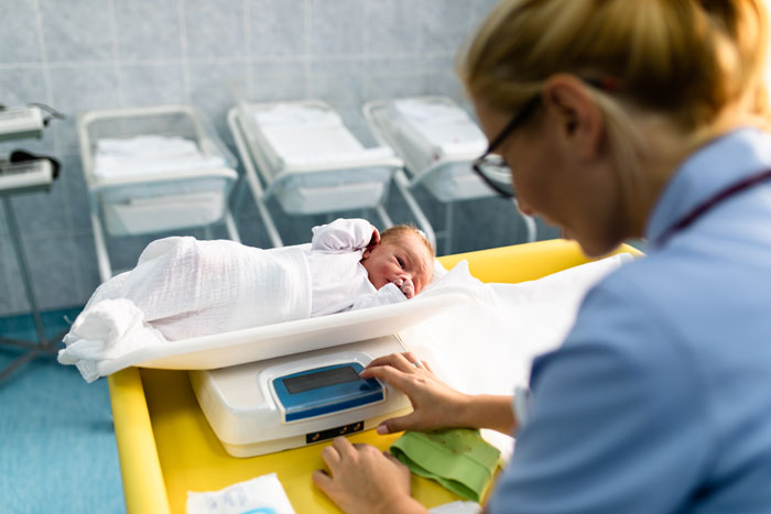 Nurse weighing newborn baby on digital scale in hospital nursery