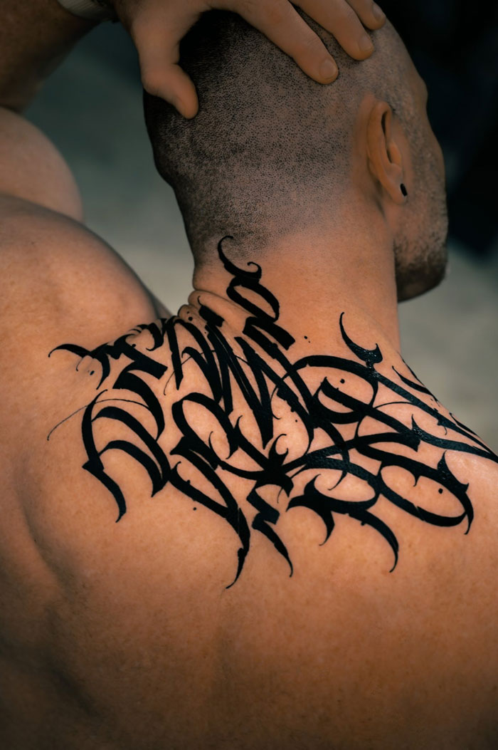 A tattoo artist's talent is evident in this elaborate black script tattoo on a man's back, a questionable idea.
