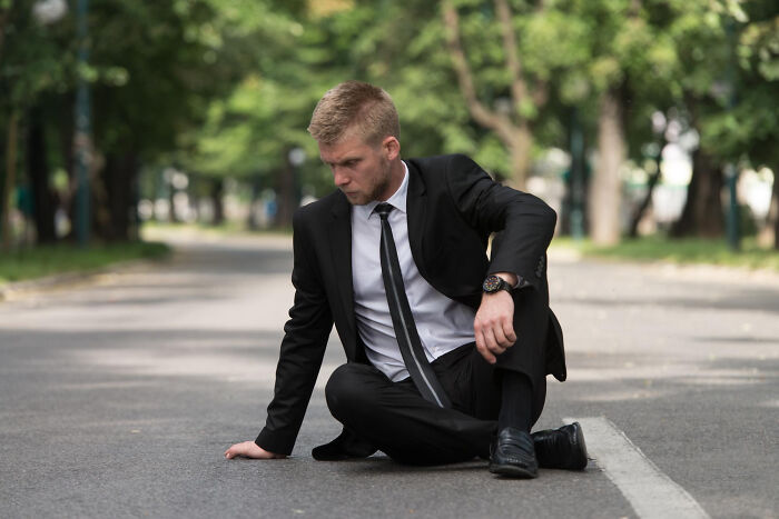 Man in suit sitting on road looking unsettled