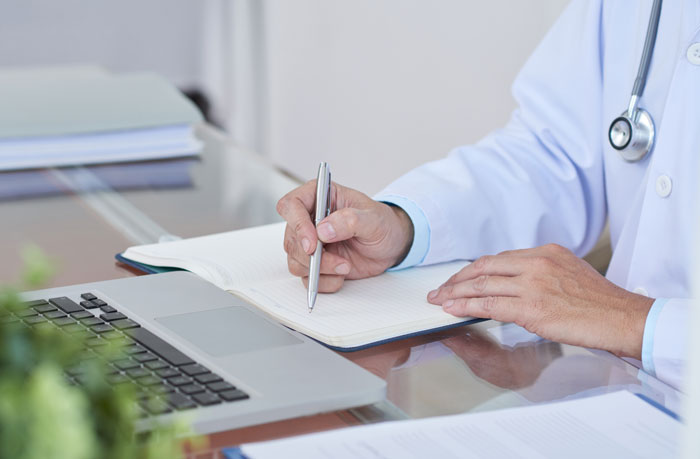 Doctor writing notes at laptop in medical office with stethoscope