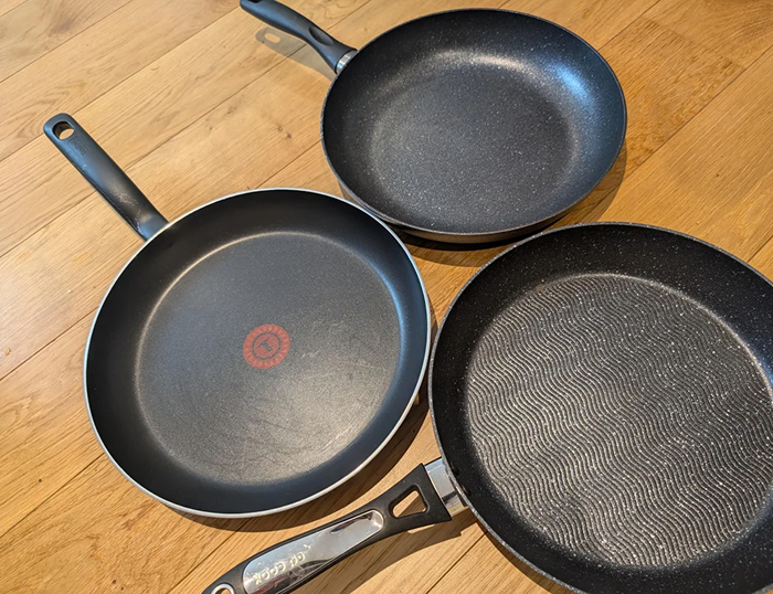 Three non-stick frying pans on a wooden surface, illustrating cooking myths about cookware