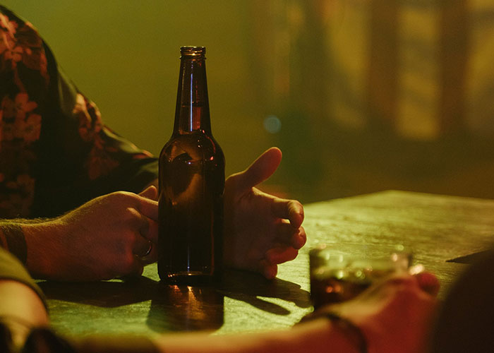 Close-up of hands and beer bottle on table in dim bar setting
