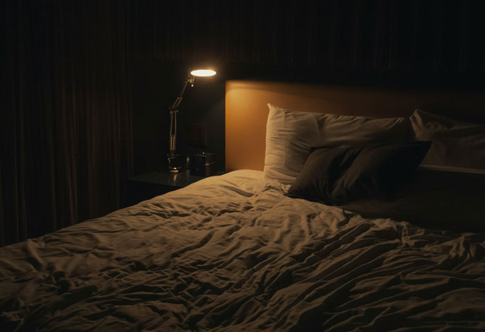 Dark bedroom with bed, pillows, and lit bedside lamp