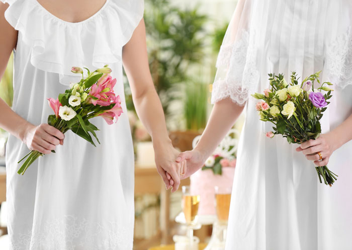 Two brides in white dresses holding hands and bouquets
