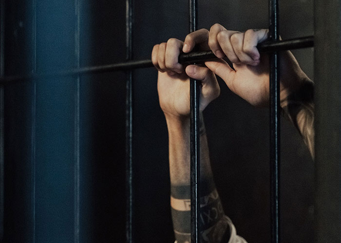 Hands gripping prison bars, symbolizing consequences for popular kids who peaked in high school