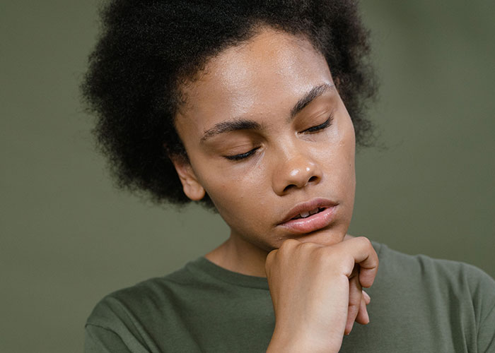 A young woman with her eyes closed and hand on her chin, reflecting on moments when kids cant keep contact with parents.