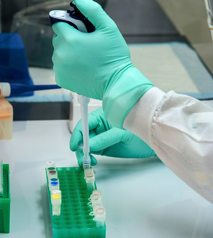A scientist in green gloves performing DNA testing with a pipette on multiple small vials.