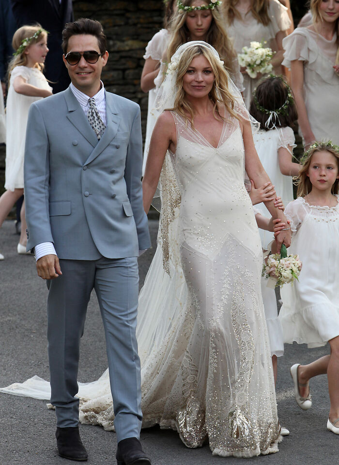 Kate Moss in a dazzling celebrity wedding dress, walking hand-in-hand with her groom and flower girls, embodying a bohemian chic wedding.
