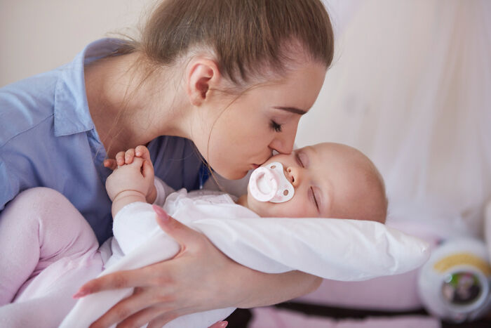 Mother kissing sleeping baby illustrating human body care