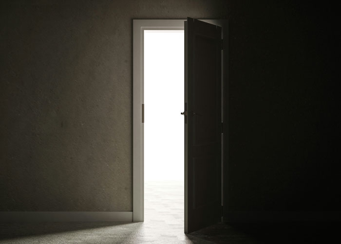 Dimly lit doorway slightly ajar leading to a bright room representing locked spare bedroom Dimly lit doorway slightly ajar leading to a bright room representing locked spare bedroom