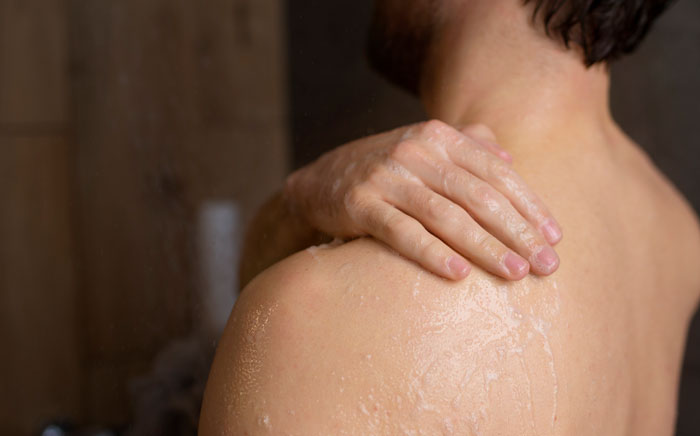 Man washing or scrubbing bare shoulder in the shower