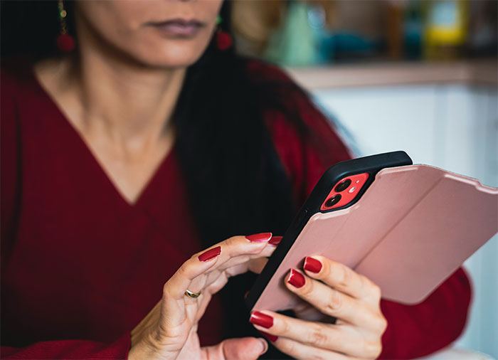 A woman in a red shirt with red painted nails scrolls on her phone, after being told to leave home.