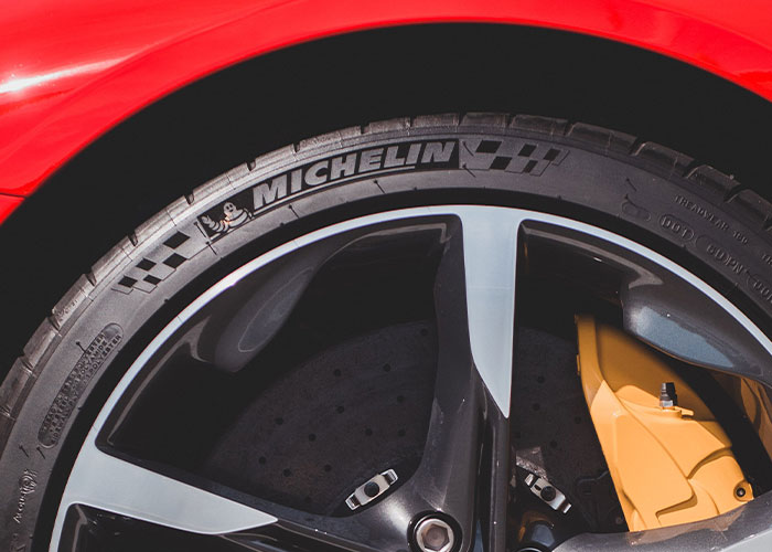 A close-up of a Michelin tire on a red car wheel with yellow brake calipers, a serious problem solved with quality.