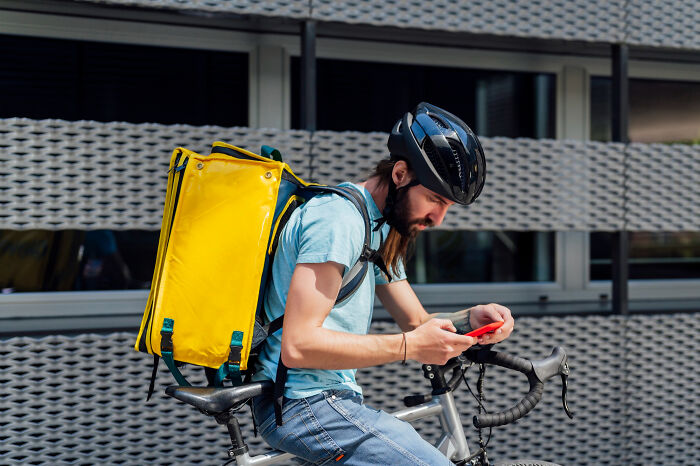 Cyclist wearing helmet checking phone with yellow delivery bag modern world audacity