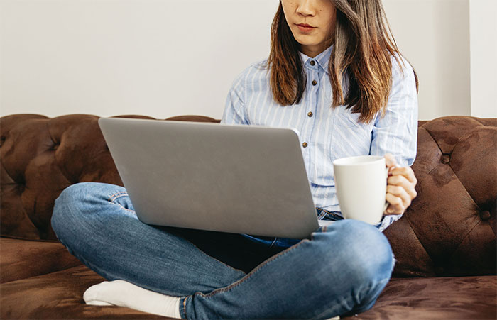 A woman sits on a couch with a laptop and mug, perhaps reflecting on being told to leave home.
