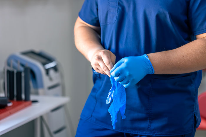 Medical worker putting on blue disposable gloves in clinic