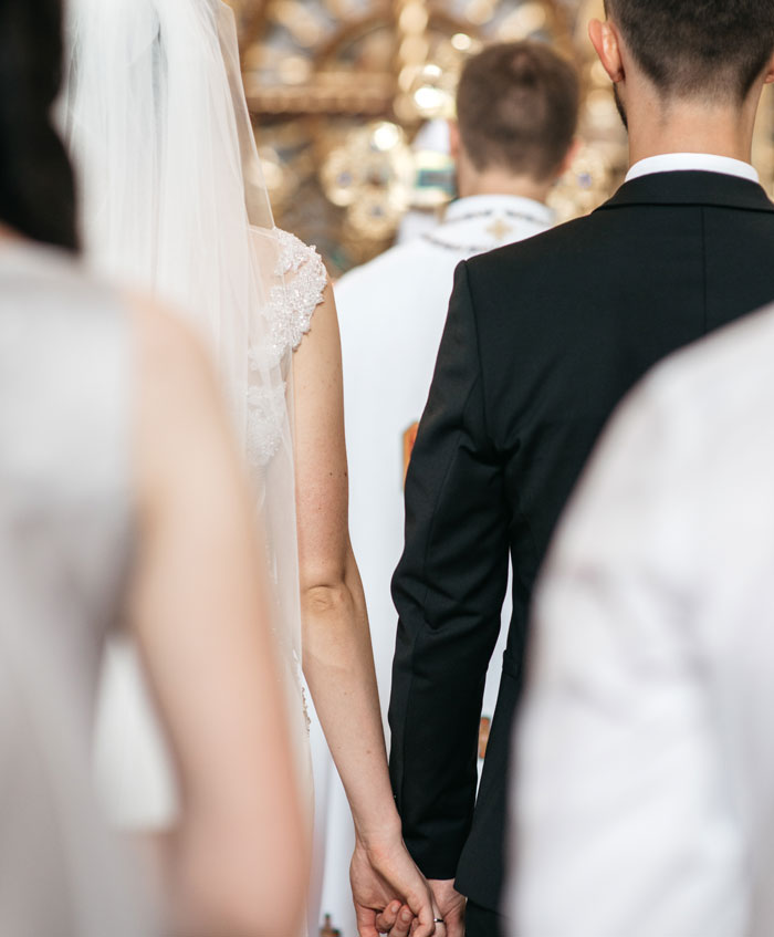 Wedding couple holding hands during ceremony with priest in the background