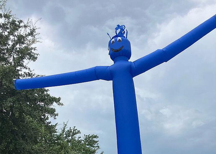A tall, blue inflatable tube man with a happy face, waving its arms against a cloudy sky, representing unserious solutions.