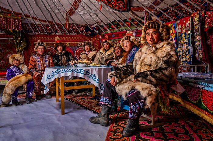 A family in traditional fur clothing gathered around a table in a decorated yurt, a cultural photo from the 2025 Chromatic Awards.