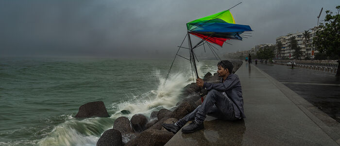 A man with a broken colorful umbrella sitting by the sea during a storm, from the Chromatic Awards.