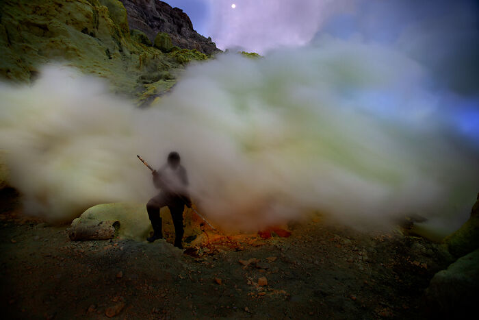 A person shrouded in smoke amidst a volcanic landscape, a striking photo from the Chromatic Awards.