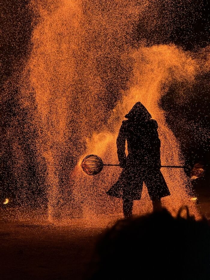 A hooded figure standing amidst a cascade of fire sparks, a captivating photo from the 2025 Chromatic Awards.