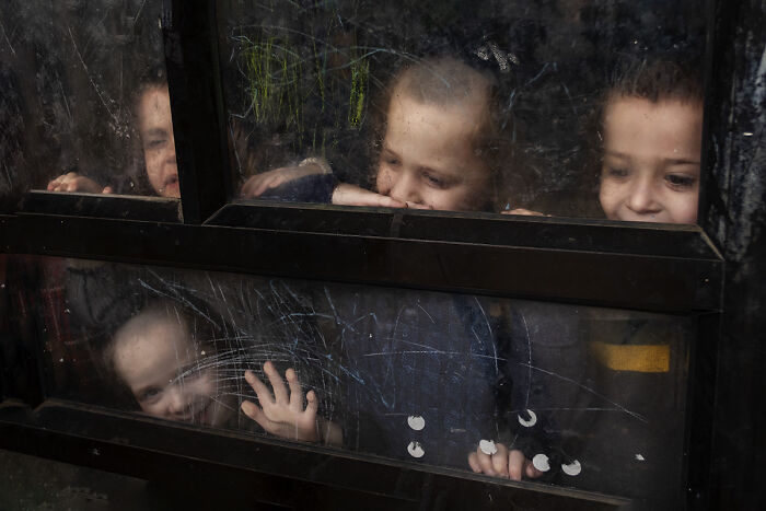 Four children peer through a grimy window, a compelling photo from the 2025 Chromatic Awards telling stories of people.