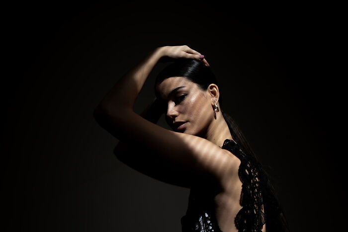A woman with dark hair poses in dramatic light with shadows striped across her face, from the 2025 Chromatic Awards.
