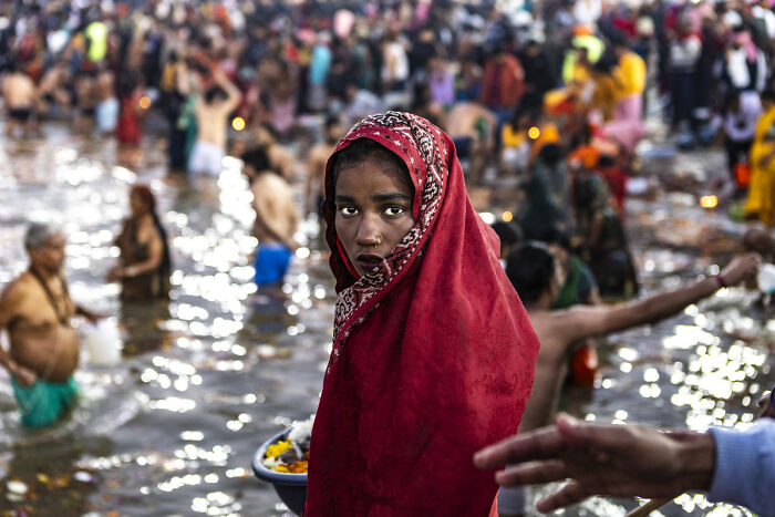 A young girl in a red headscarf stands in water amidst a crowd, a powerful image from the Chromatic Awards.