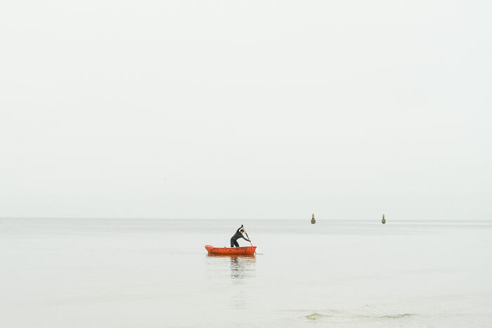 A lone person in a red boat on a calm, misty sea, a poignant photo from the 2025 Chromatic Awards, telling stories.