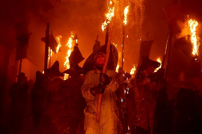 People in dark attire holding flaming torches in a dramatic, fire-lit scene, from the Chromatic Awards.