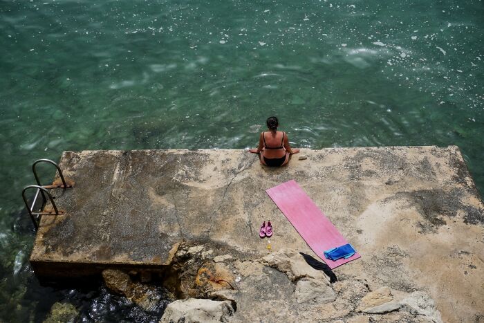 A person meditating by the water on a concrete pier, a powerful image from the 2025 Chromatic Awards, telling stories.