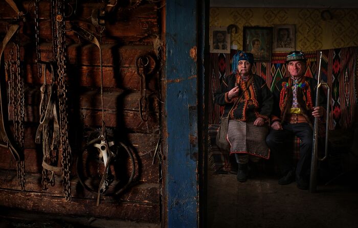 An elderly couple in traditional attire sits in a rustic room, a 2025 Chromatic Awards photo telling stories of people.