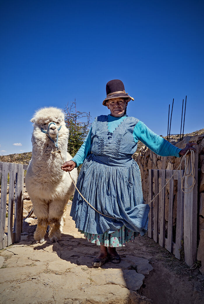 An older woman with an alpaca under a bright blue sky, featured in the 2025 Chromatic Awards, telling stories.