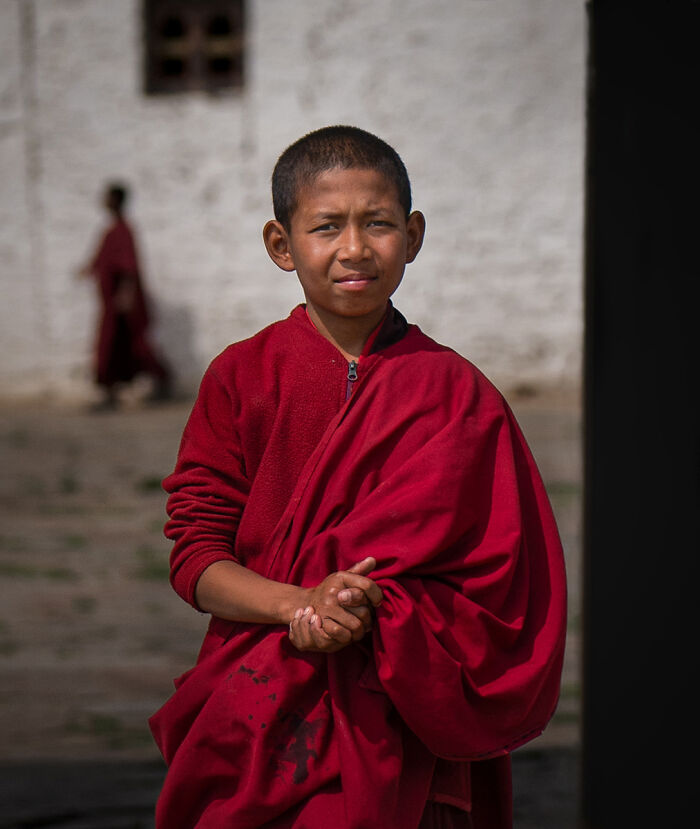A young monk in red robes looking at the camera, a compelling portrait from the 2025 Chromatic Awards, telling stories.