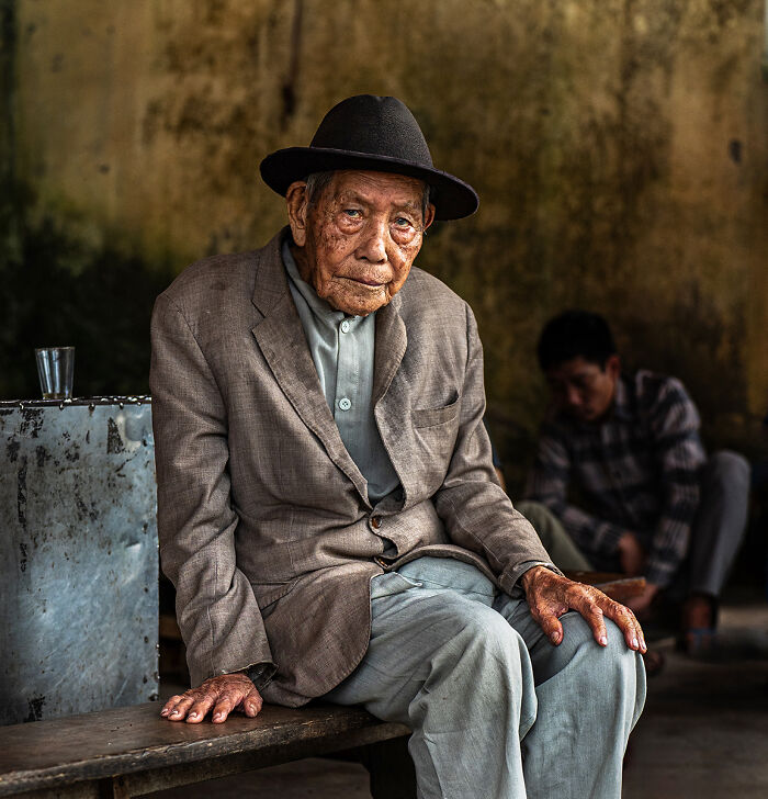 Elderly man in a hat sits on a bench, a compelling photo from the Chromatic Awards telling stories of people.