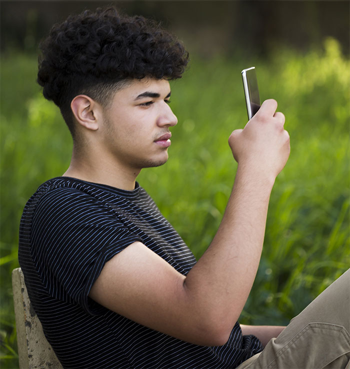 A young man looking at his phone in a grassy outdoor setting, relating to the story of a woman refusing to follow a rule.