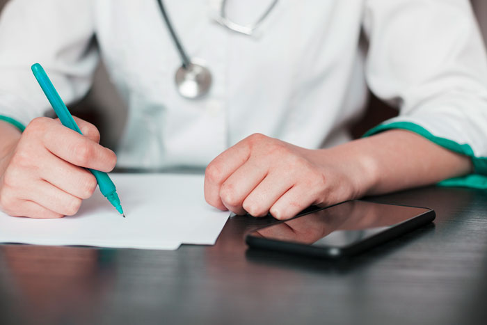 Doctor writing notes with tablet on desk in clinic