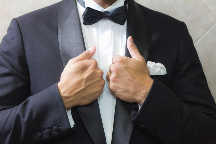 Groom adjusting tuxedo jacket at wedding with bow tie