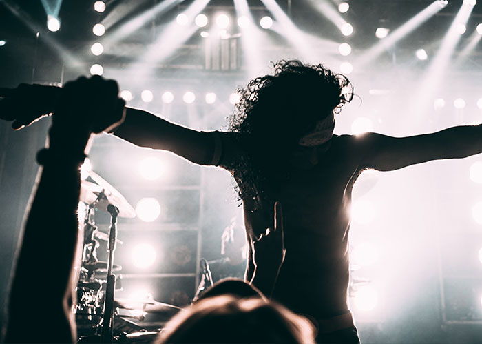 Musician on stage with arms outstretched under bright lights, symbolizing the peak of popular kids in high school.