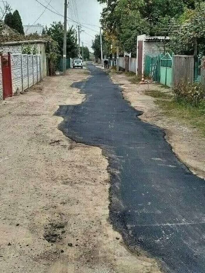 A narrow strip of fresh asphalt covering only the middle part of a dirt road, an example of Slavic Science.