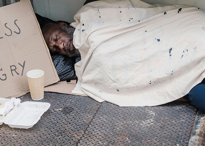 Homeless man sleeping on street with sign about legal offense