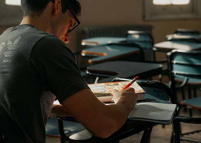 Student in glasses takes notes in a classroom, reflecting on the academic journey of popular kids.