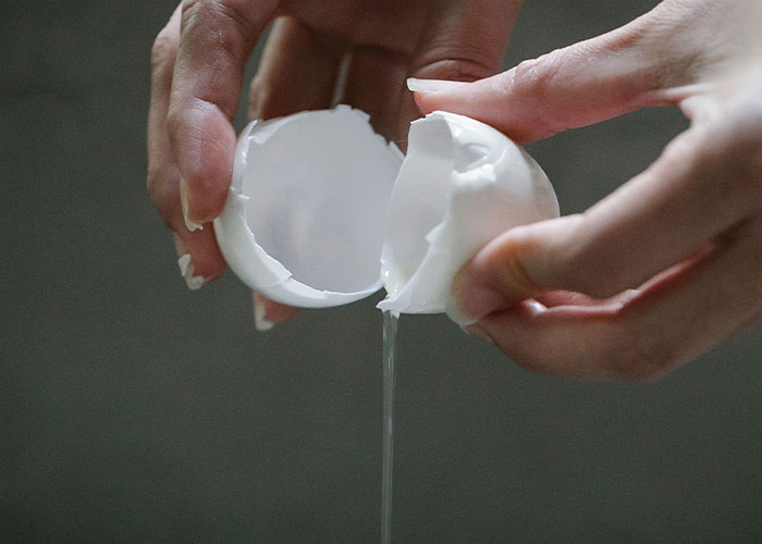 A pair of hands separating a cracked eggshell, with the egg white dripping. This image shows problem-solving.