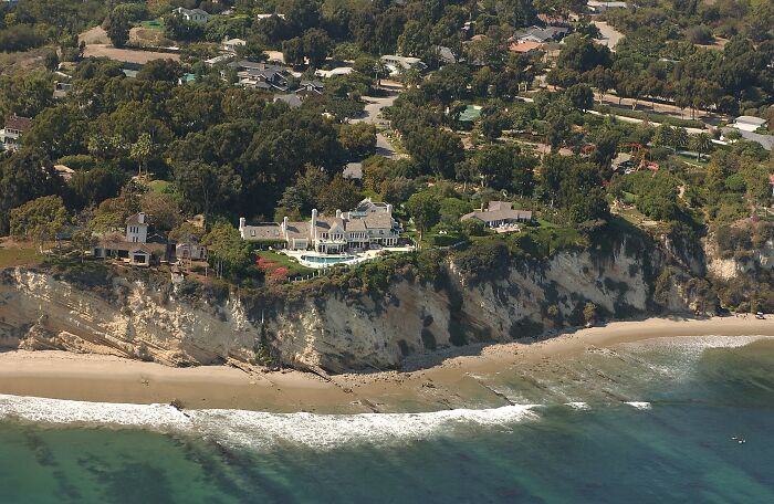 A grand mansion on a cliff overlooking the ocean, hinting at celebrity scandals and luxurious lives.