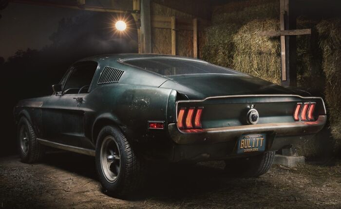 Rear view of a classic dark green Ford Mustang, famous for its role in an unsolved mystery, parked in a barn.